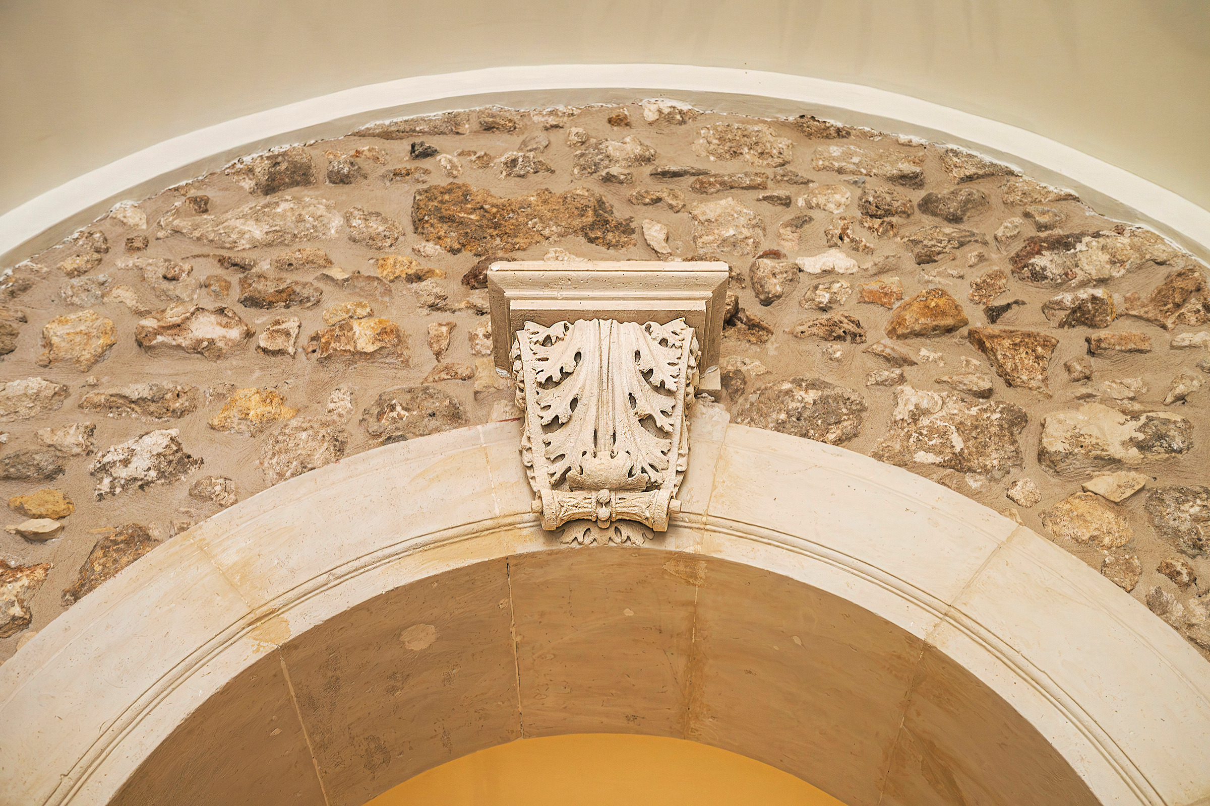 Portale ad arco in pietra con stemma scolpito sulla chiave, fra murature storiche a vista.