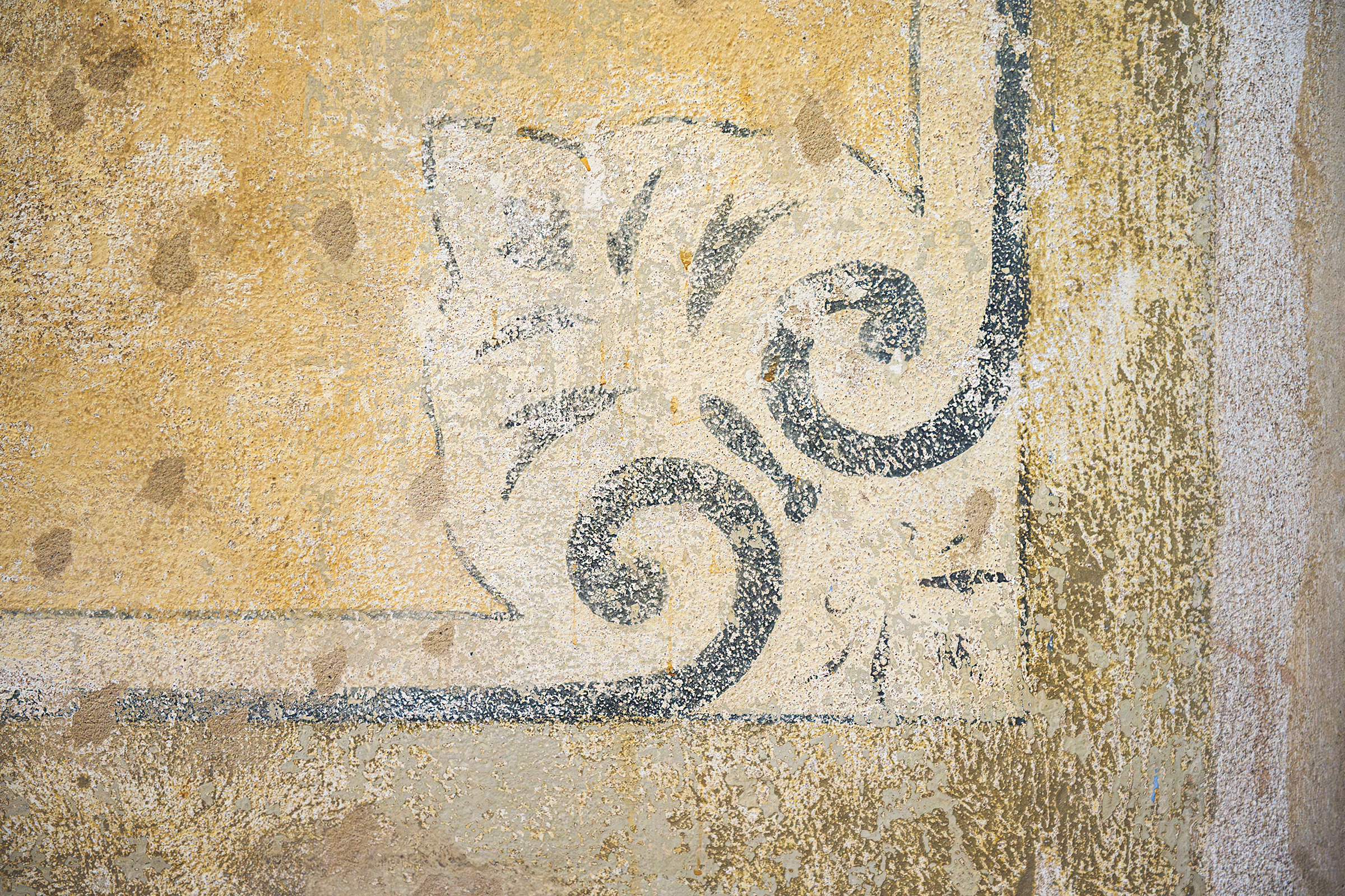 Dettaglio di una decorazione dipinta restaurata, con motivi a volute e tracce delle superfici storiche.