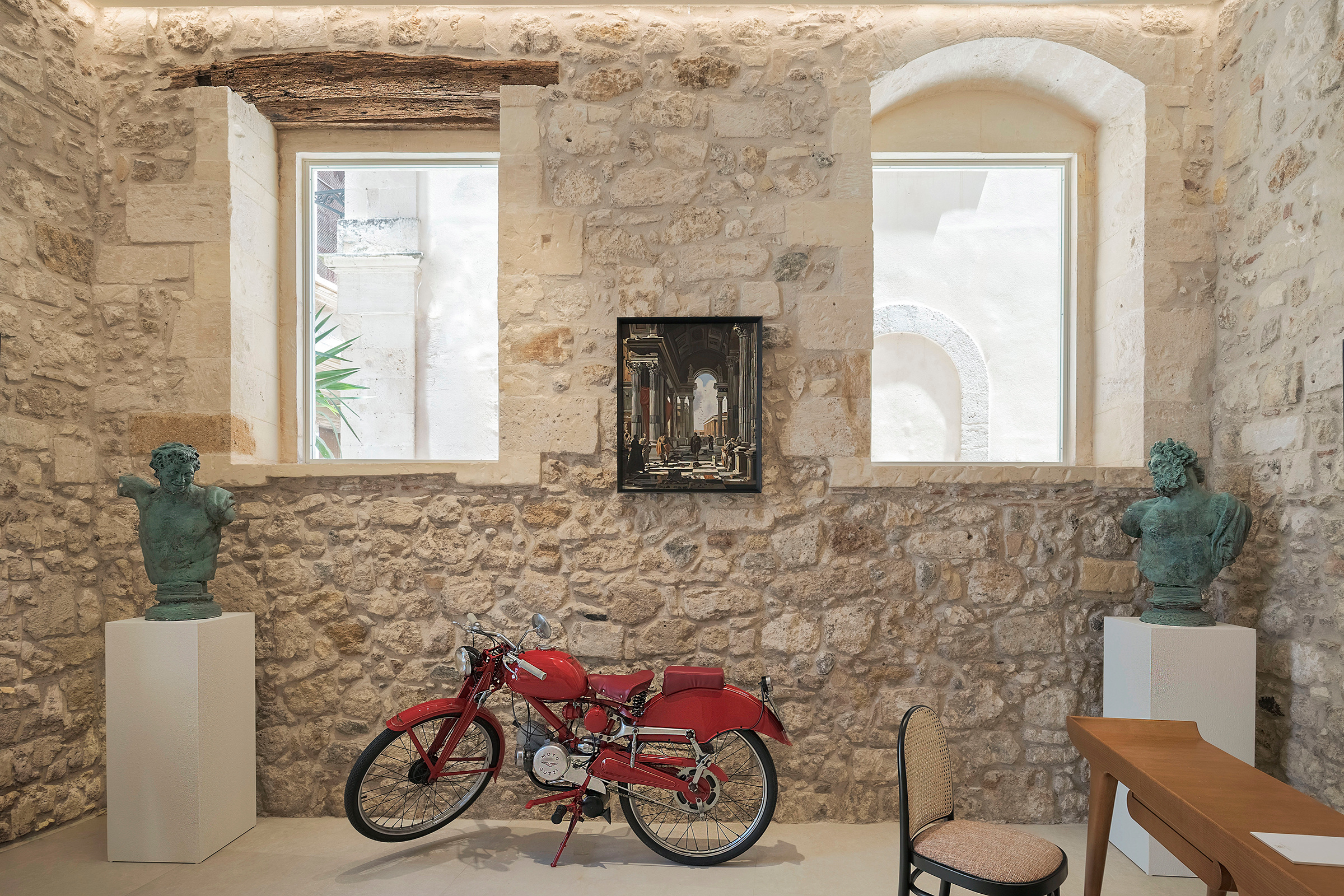 La Moto Guzzi Guzzino rossa esposta fra due busti nella galleria di Cool Dreams.