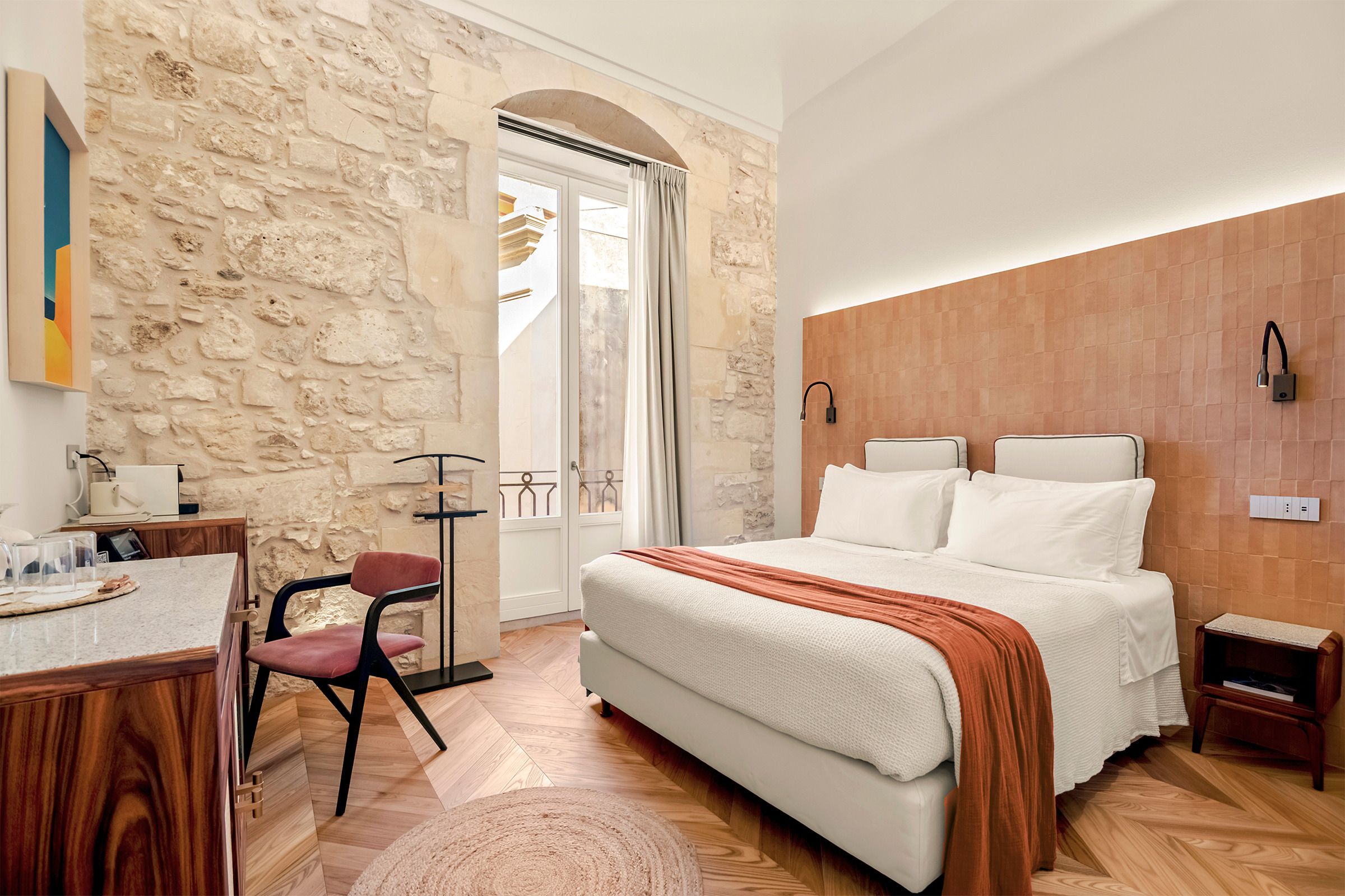 Camera Comfort con letto, parete in pietra, finestra ad arco e scrittoio in legno e midollino.