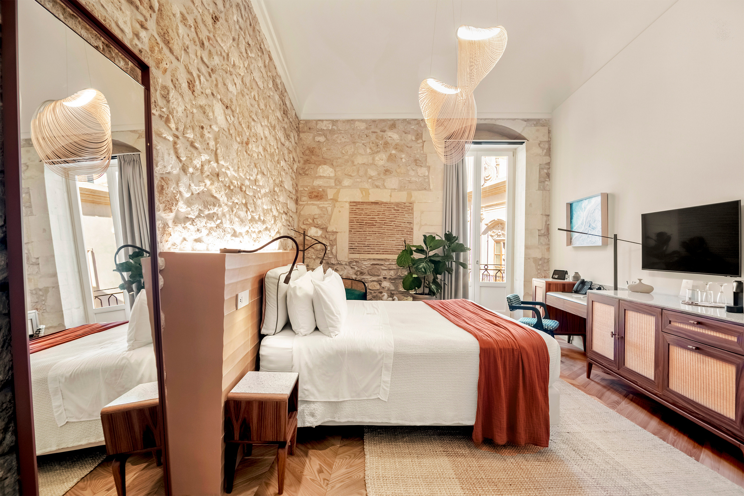 Camera Deluxe con parete in pietra, letto, sospensioni leggere e mobili in legno e midollino.