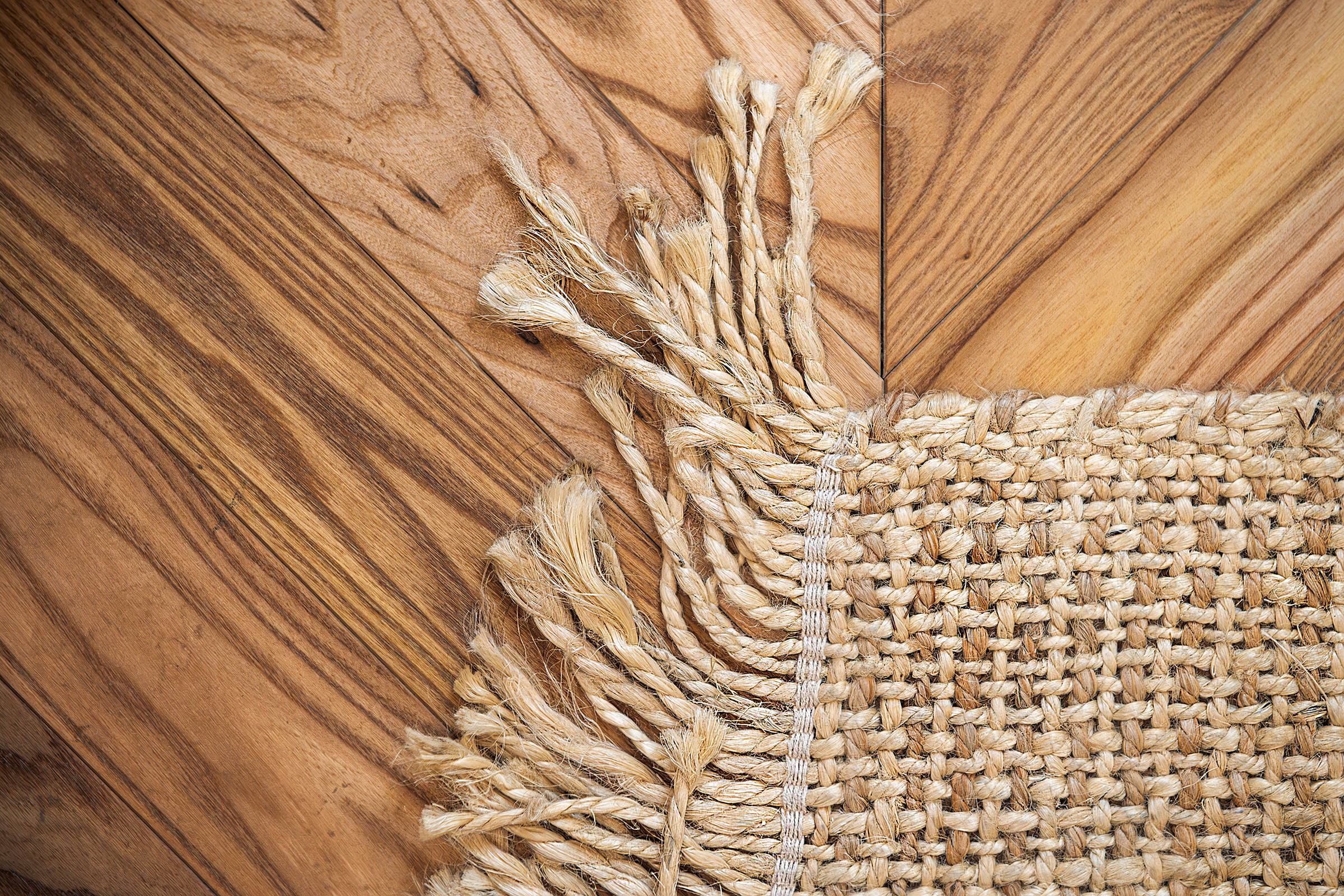 Intreccio e frange di un tappeto sul parquet in olmo posato a spina.