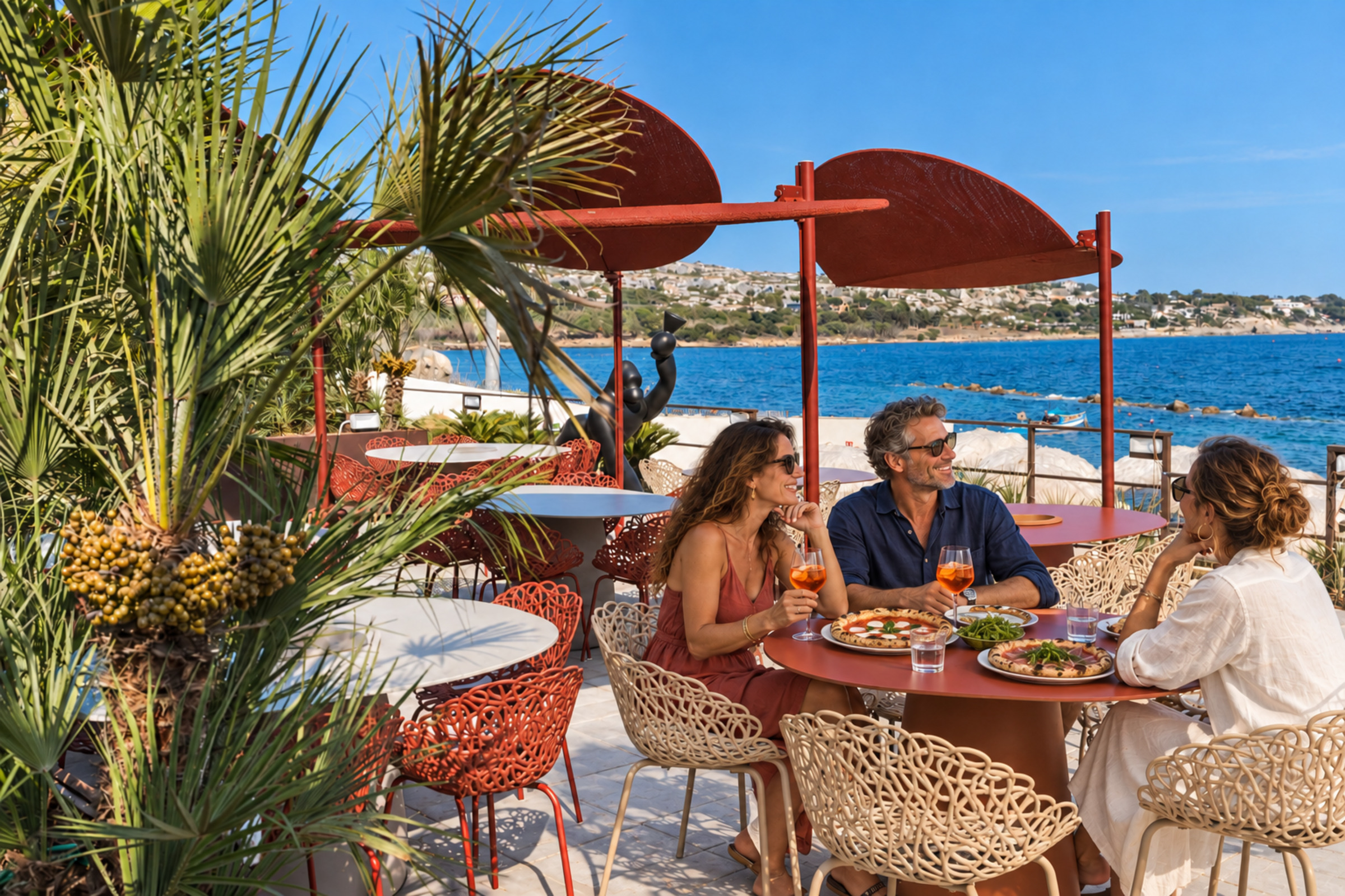 Tre ospiti mangiano la pizza a un tavolo all’aperto vicino al mare.